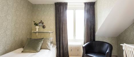 A bedroom with a bed, a chair, a radiator, and a window with curtains.