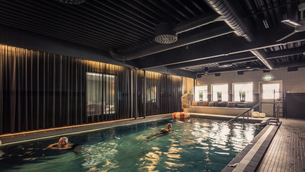Una piscina interior con diseño moderno, incluyendo techo y paredes oscuras, y un área de estar con vistas a la piscina.