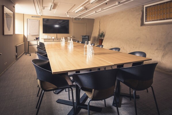 Un salón de conferencias con una larga mesa, sillas negras, una pizarra y una pantalla de televisión.