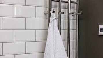 Una toalla blanca colgada en un perchero metálico en un baño con paredes de azulejos blancos y una pared de acento marrón oscuro.