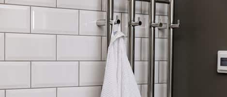 A white towel hanging on a metal towel rack in a bathroom with white tiled walls and a dark brown accent wall.