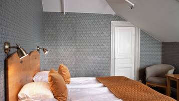 Ein Schlafzimmer mit einem Holz-Kopfteil, einem Bett mit weißer und brauner Bettwäsche, einer braunen Steude, einem Sessel und einer weißen Tür.