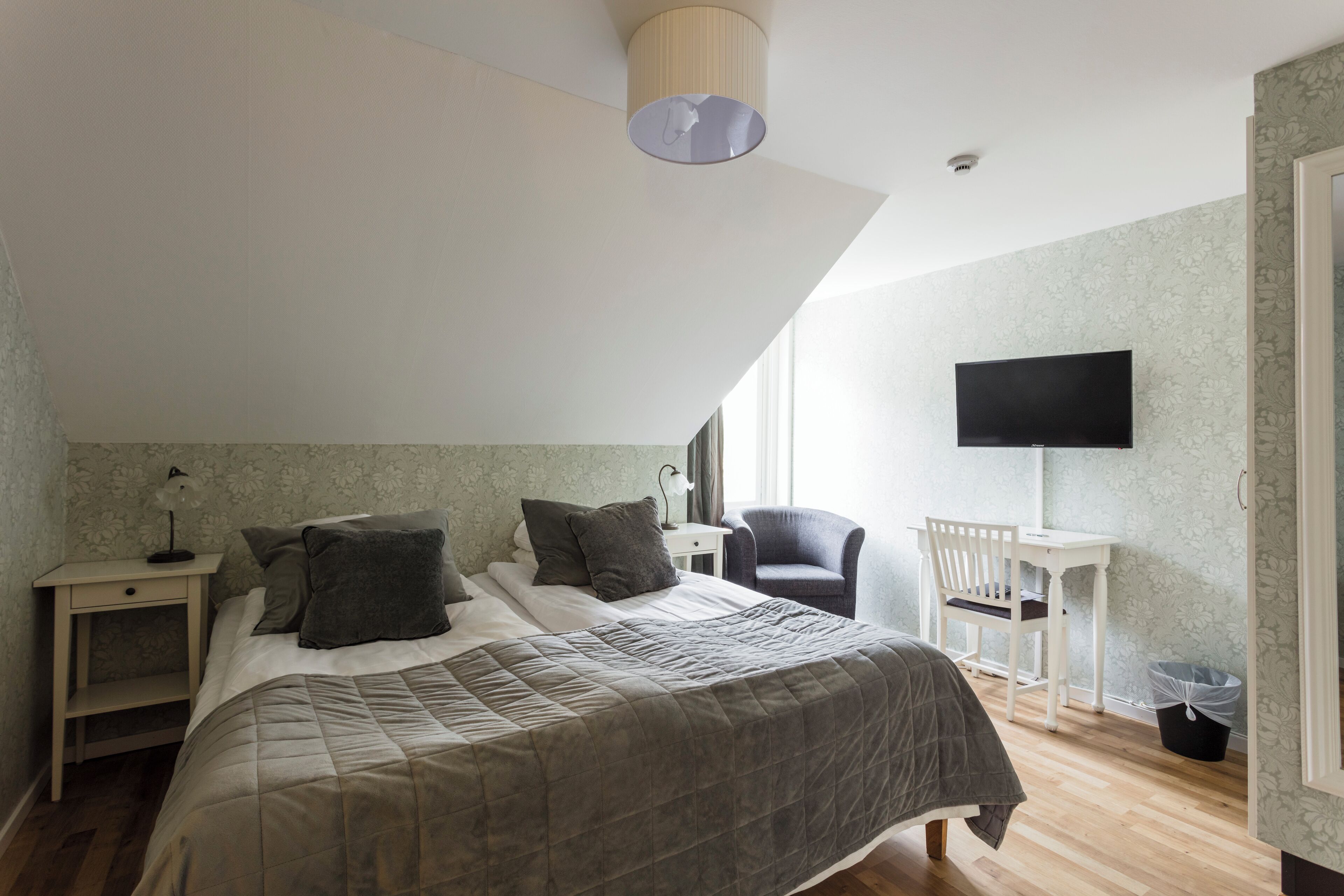 A bedroom with a large bed, a desk, a chair, and a TV on the wall.