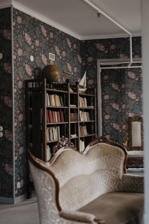 A room with a floral wallpaper, a bookshelf, and a vintage armchair.