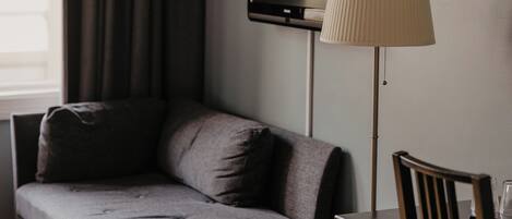 Una habitación moderna con sofá gris, una lámpara de pie, televisor de pantalla plana y una mesa de comedor de madera.