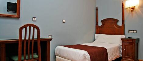 A bedroom with a wooden bed, a desk with a chair, a nightstand, and a wall-mounted lamp.
