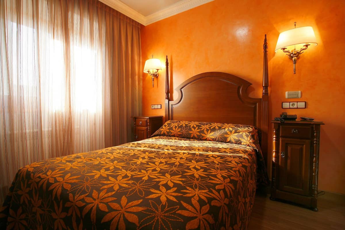 A hotel room with a large bed, two wall-mounted lamps, a wooden nightstand, and a cabinet.