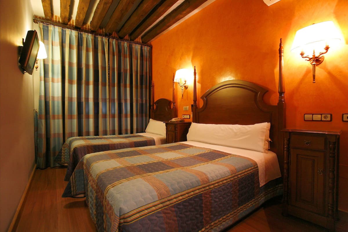 A hotel room with two beds, a wooden headboard, a nightstand, and a lamp.