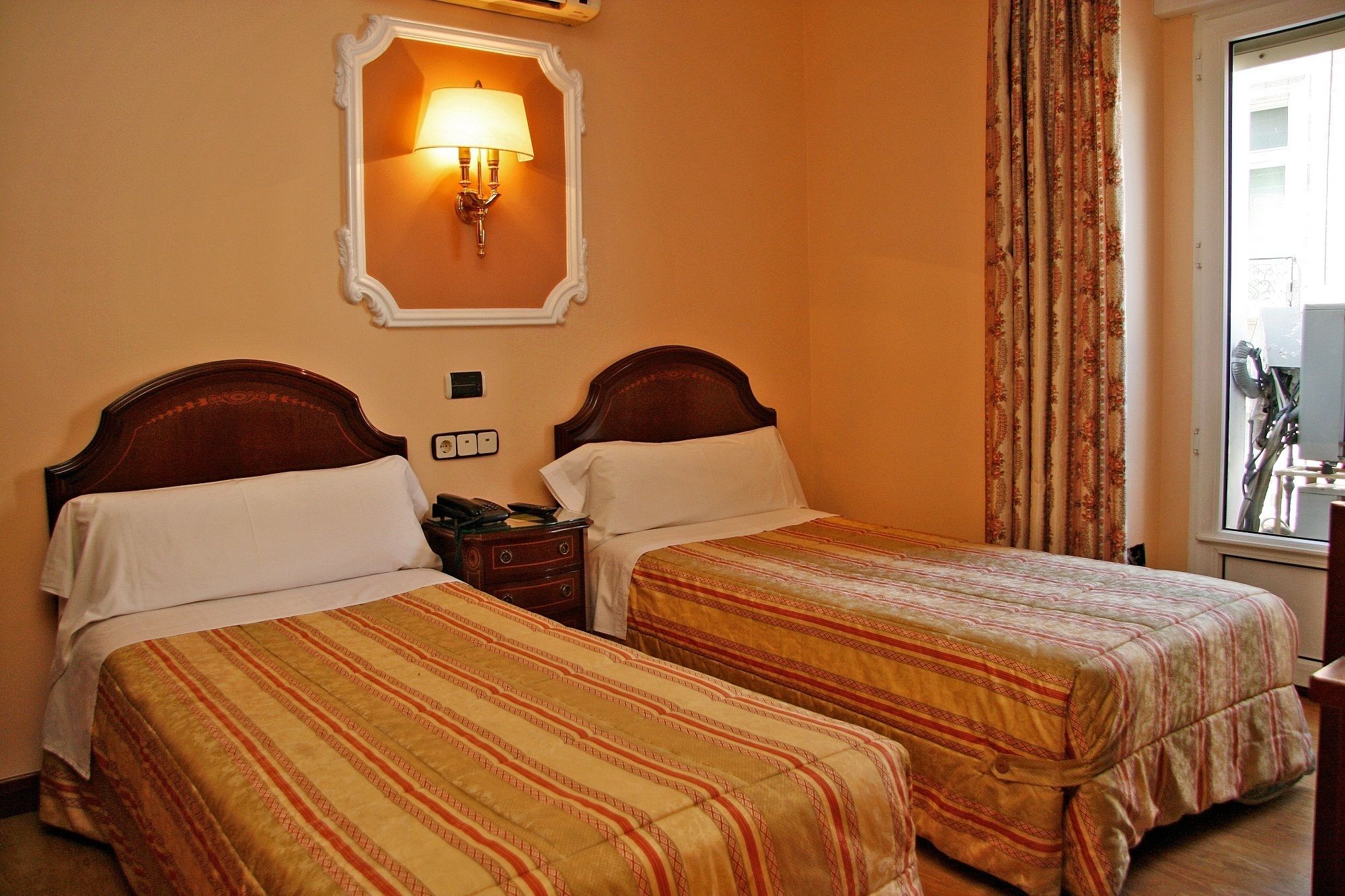 Two single beds with matching headboards and footboards, a bedside table with a lamp, and a window with curtains.