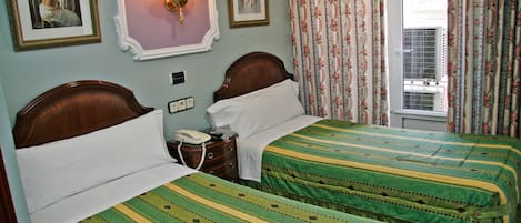 A hotel room with two single beds, a bedside table with a lamp, a phone, and a wall-mounted light fixture.