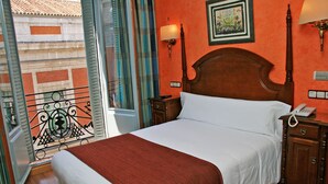 Een hotelkamer met een houten bed, wit beddengoed, een rode plaid, een nachtkastje met een telefoon en een wandlamp.
