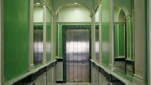 Een gang met groene wanden en een marmeren vloer, die leidt naar een lift.