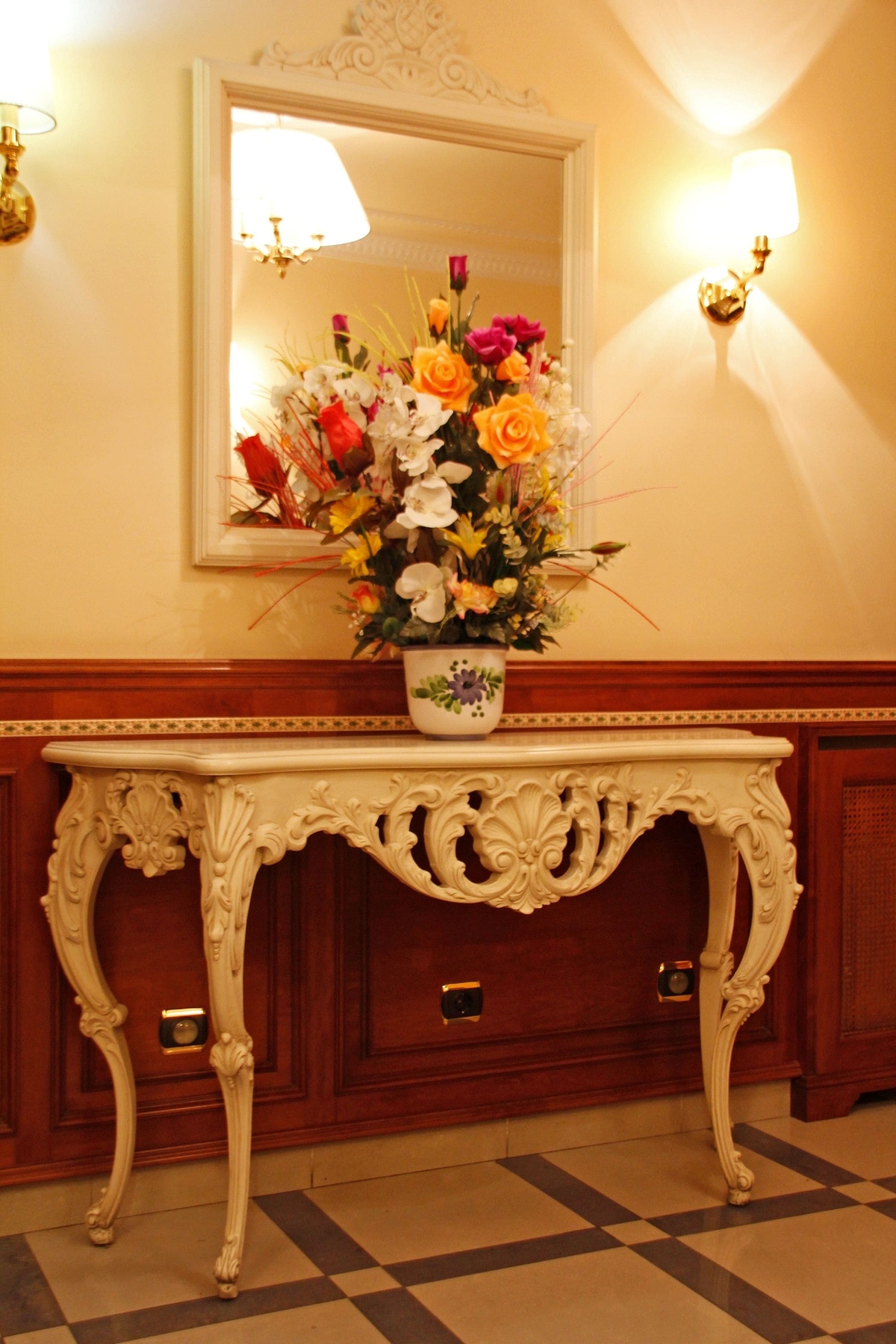 A white ornate console table with a floral arrangement in a white pot.