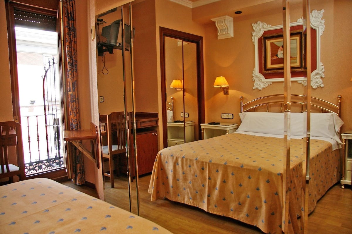 A hotel room with a bed, a desk, a chair, a nightstand, and a mirror.