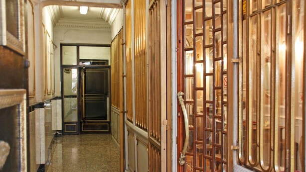 Ein Korridor mit Holztüren und Fliesenboden, der zu einem Raum mit einem großen Fenster führt.