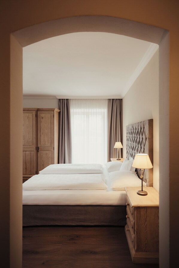 Habitación de hotel con una cama grande, un armario de madera, una mesita de noche con lámpara y vistas al exterior a través de la ventana.