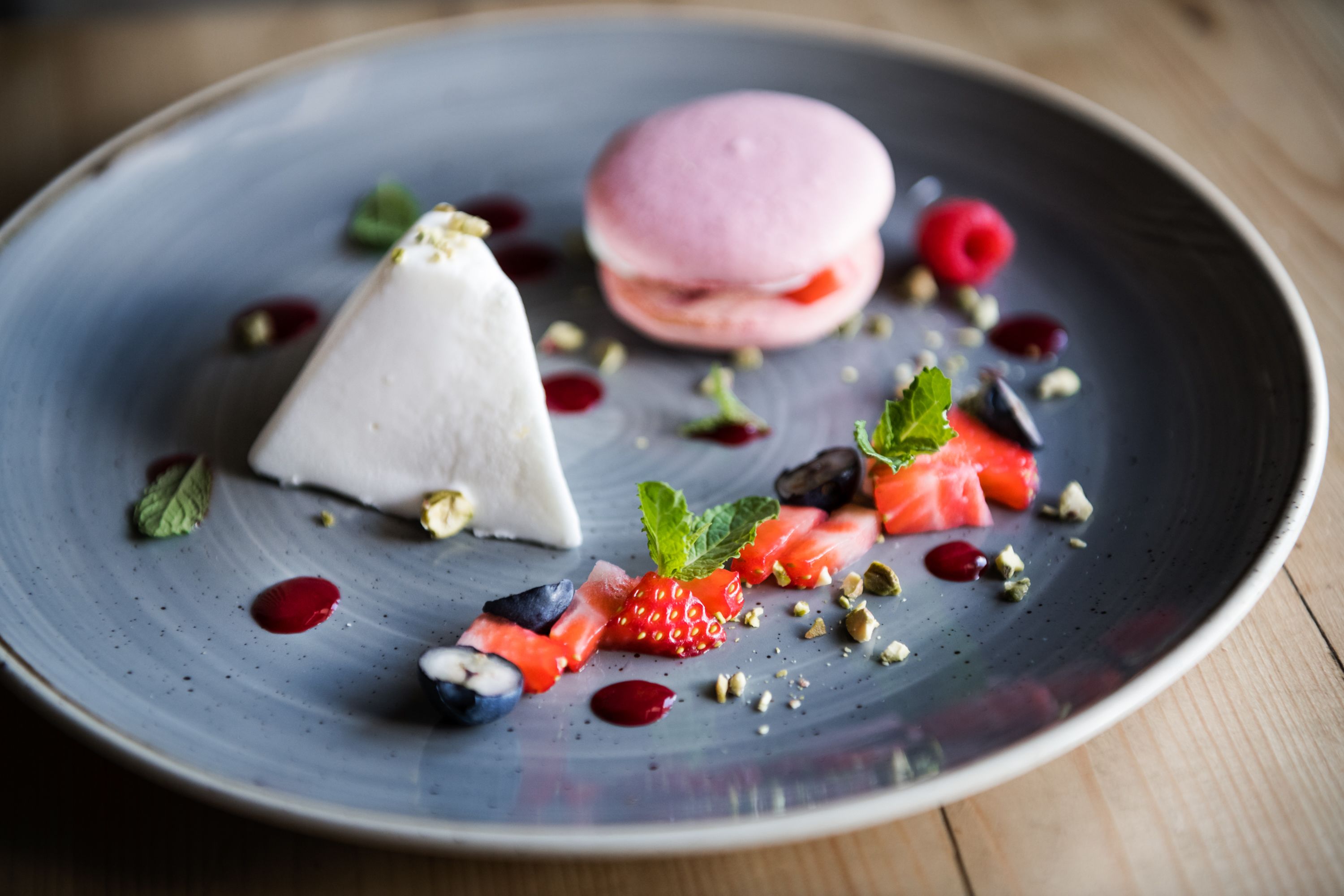 Un piattino da dessert con una pallina bianca, un macaron rosa e diversi frutti di bosco e noci.