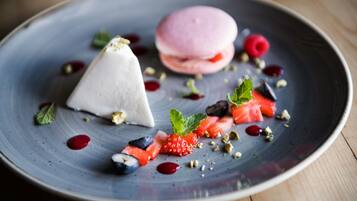 Un piattino da dessert con una pallina bianca, un macaron rosa e diversi frutti di bosco e noci.