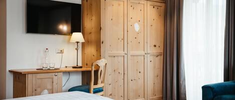 Habitación de hotel con un armario de madera, un televisor montado en la pared, un escritorio con lámpara, dos camas y una silla.