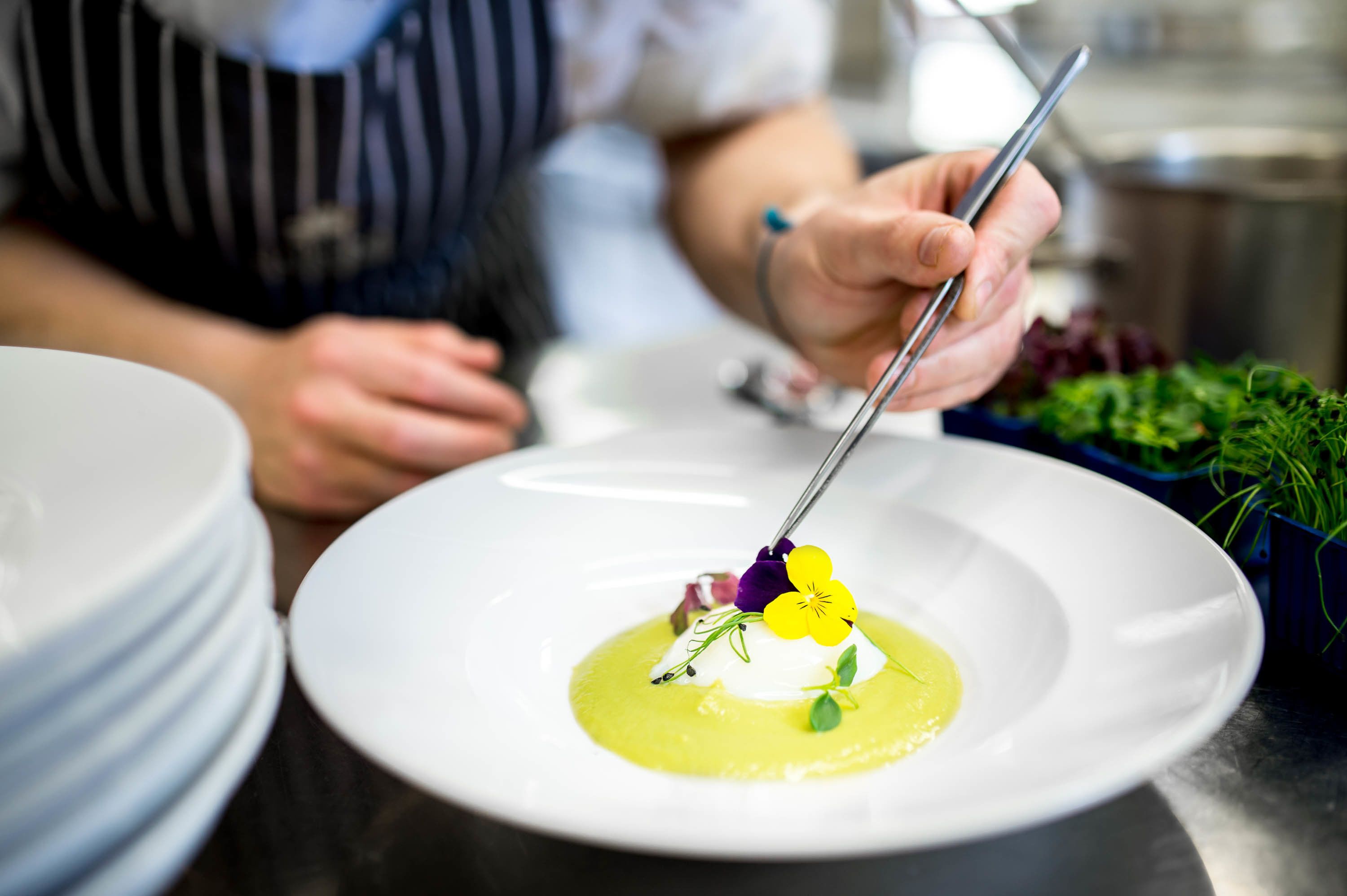 A chef preparing a dish with a spoon on a white plate.