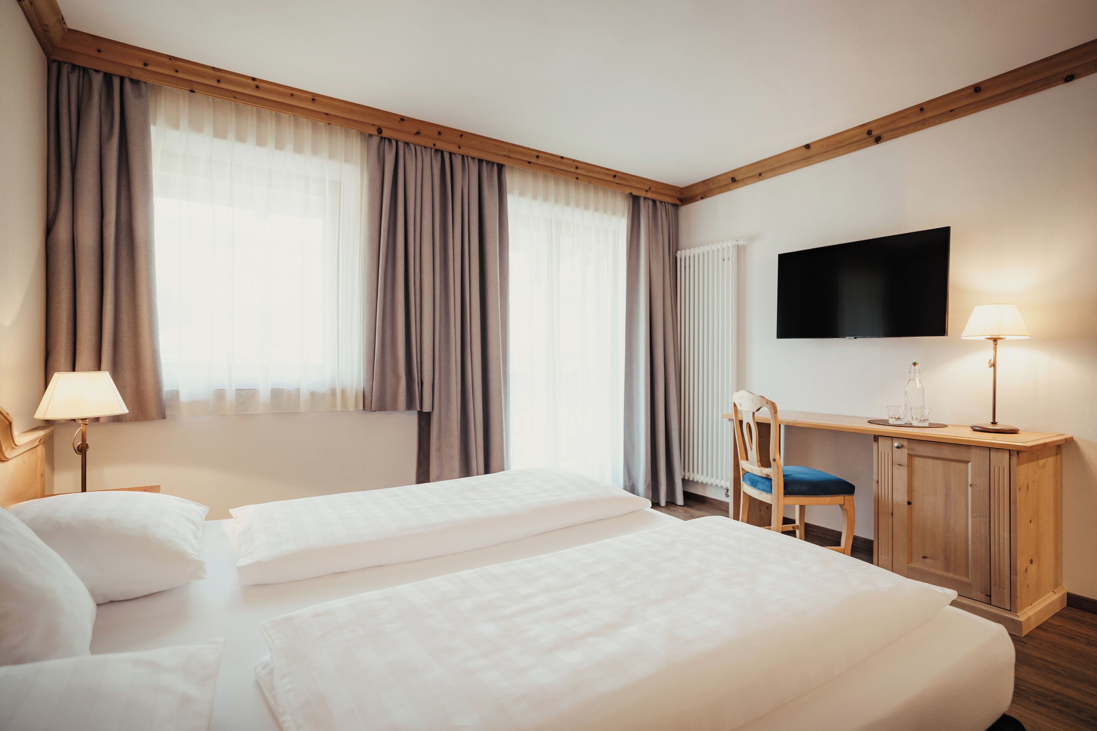 Una habitación de hotel con dos camas, un escritorio con silla, un televisor y una lámpara.