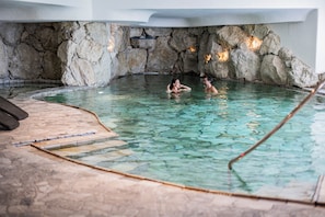 An indoor swimming pool with clear water, stone walls, and a tiled floor.