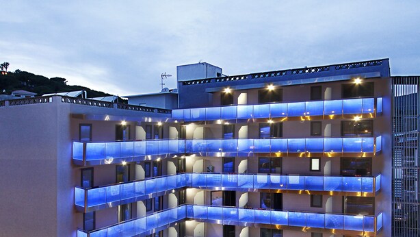 A hotel with multiple balconies, outdoor seating, and a well-lit entrance. - Summer Hotel (Calella)