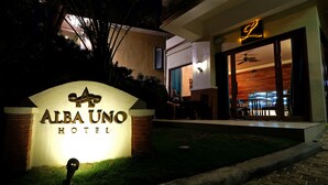 Das Hotel Alba Uno: Außenansicht mit beleuchtetem Eingang, einer Sitzgelegenheit mit Terrasse und einem sichtbaren Deckenventilator.