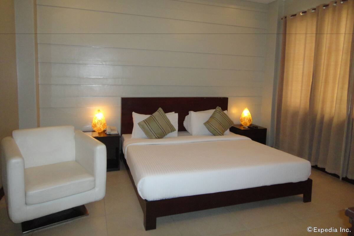 A hotel room with a bed, two bedside tables with lamps, a chair, and a curtain.