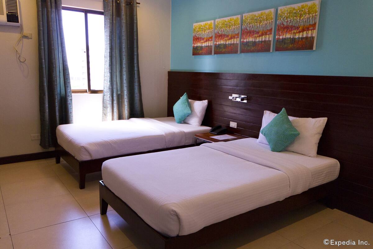 A hotel room with two beds, a wooden headboard, and a window with curtains.