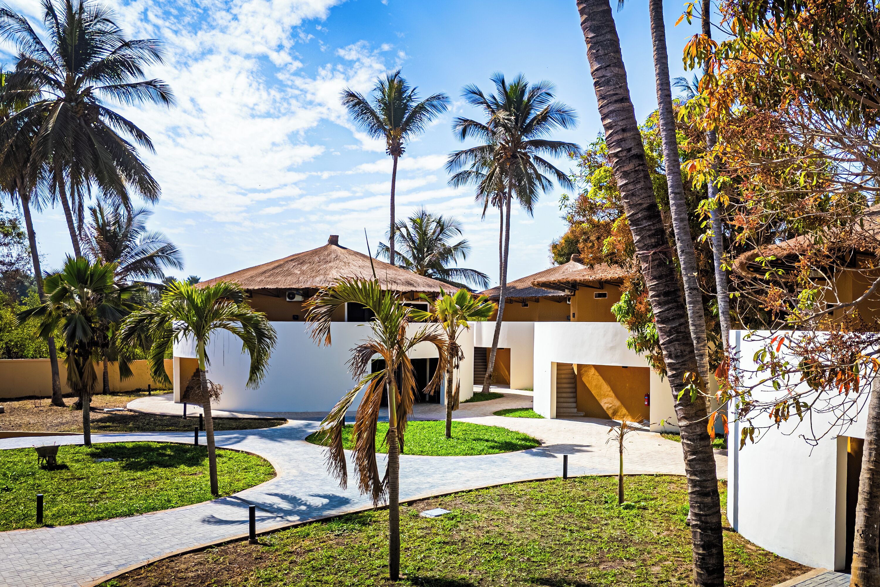 A resort with palm trees, a pathway, and a building with a thatched roof.