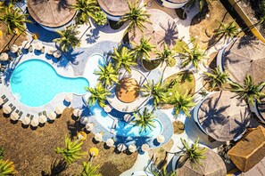 Vista aérea de un complejo turístico con piscina, palmeras y sombrillas.