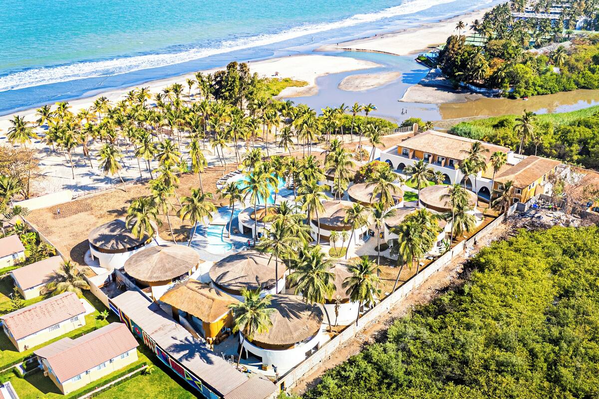 An aerial view of a resort with multiple buildings, palm trees, and a beach.