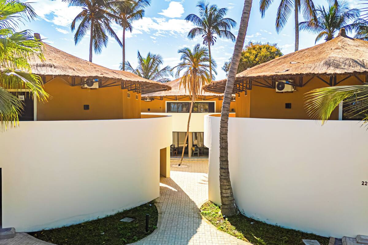 A resort with thatched-roof buildings, palm trees, and a paved walkway.