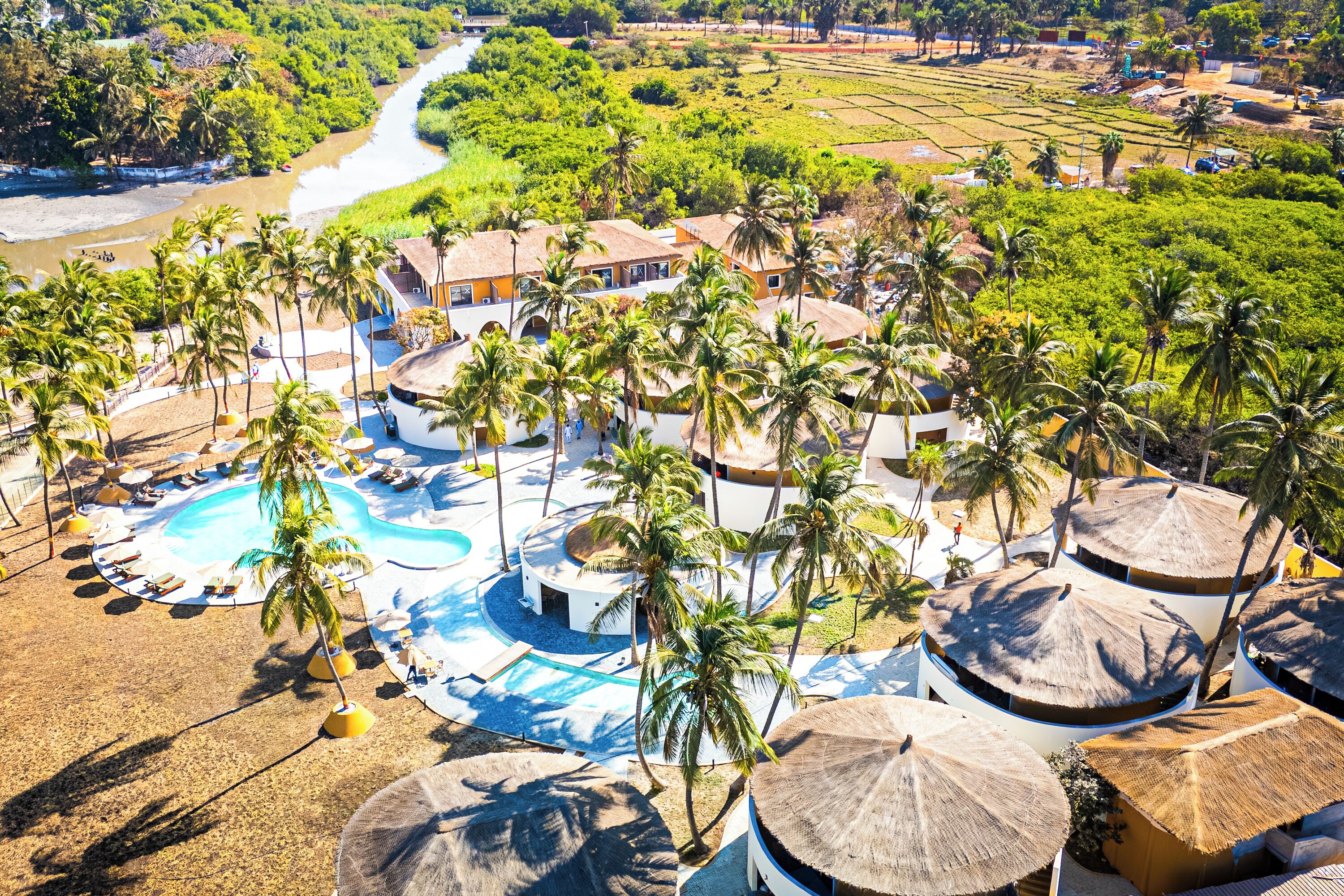Resort com vários edifícios, piscina e palmeiras.