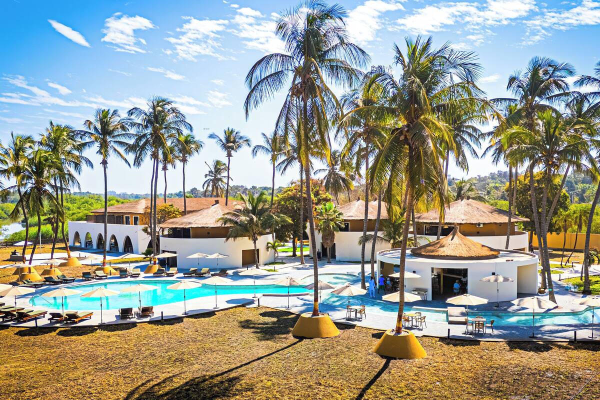 A resort with a swimming pool, palm trees, and a building with a thatched roof.