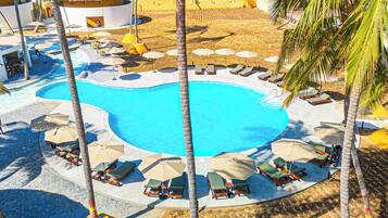 A pool surrounded by lounge chairs and umbrellas, with palm trees and a building in the background.