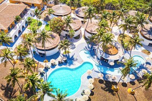 Vista aérea de un complejo turístico con varias construcciones circulares, una piscina central y palmeras alrededor.