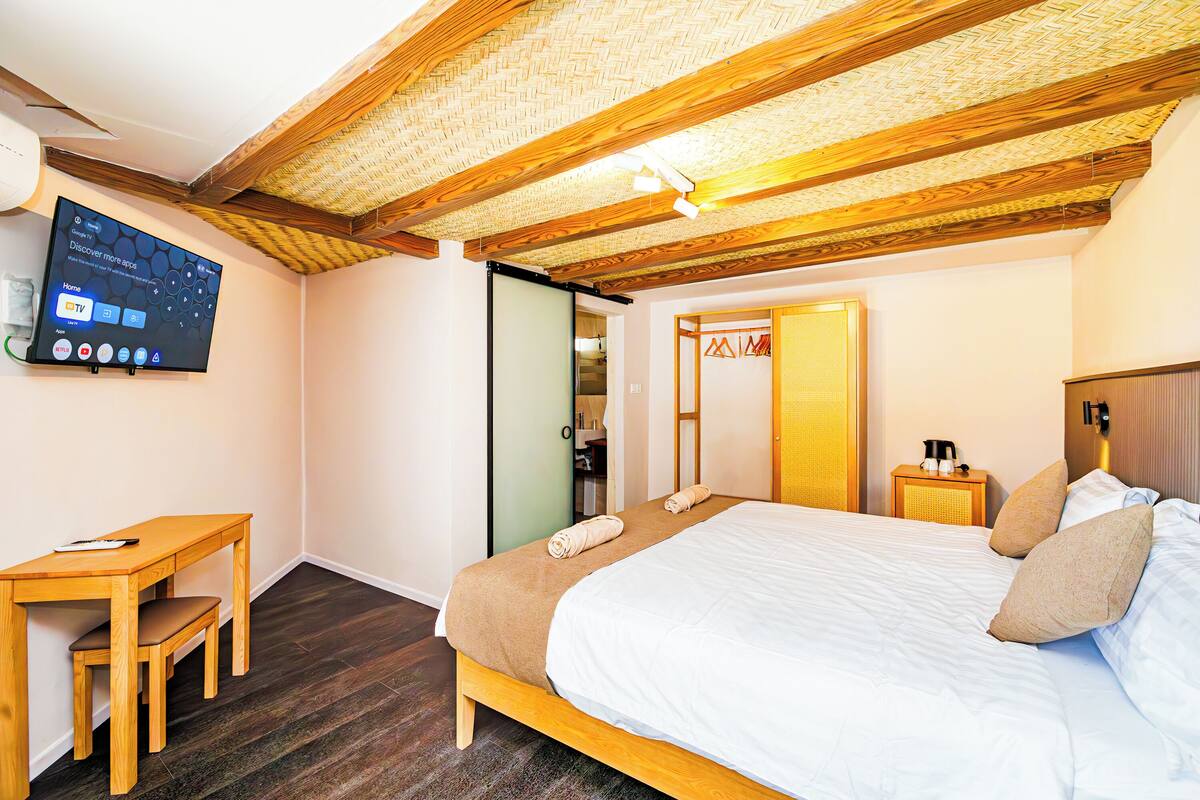 A bedroom with a bed, a desk, a chair, a TV, and a wardrobe.