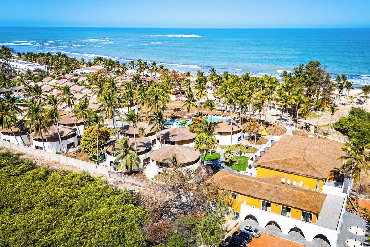 An aerial view of a coastal resort with multiple buildings, palm trees, and a beach.