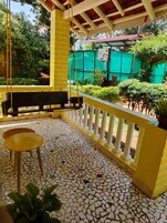 Un espacio al aire libre techado con un banco y una mesa, rodeado por una barandilla amarilla y un piso de baldosas.