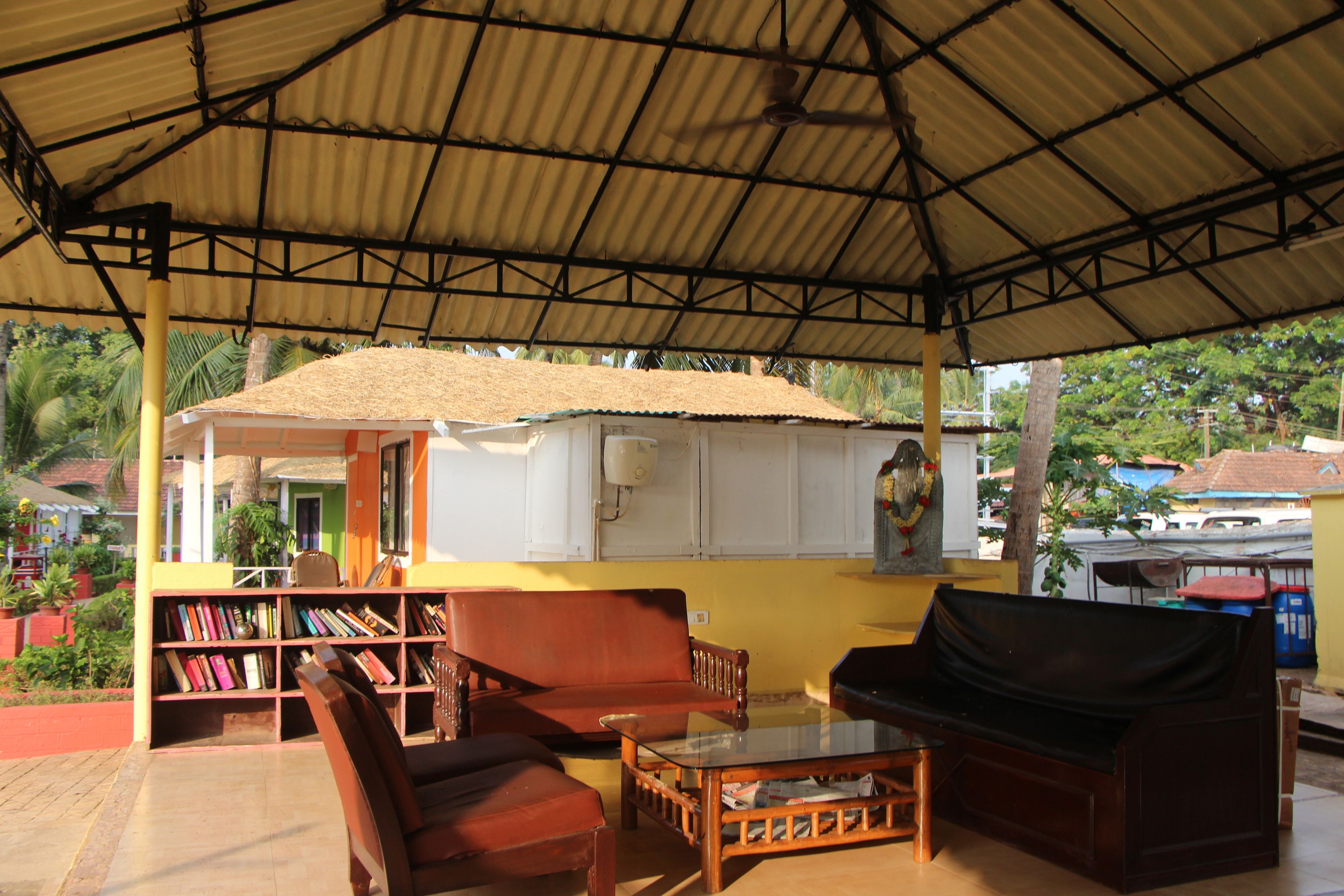 A covered outdoor seating area with a bookshelf, a sofa, and a table.