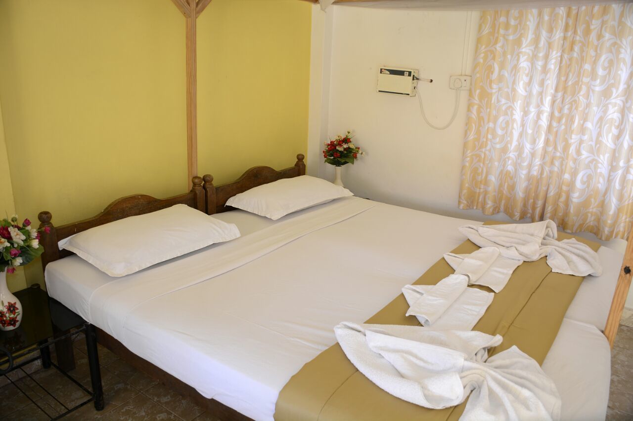 Una cama bien tendida con sábanas blancas, cabecera de madera y mesita de noche con un florero.
