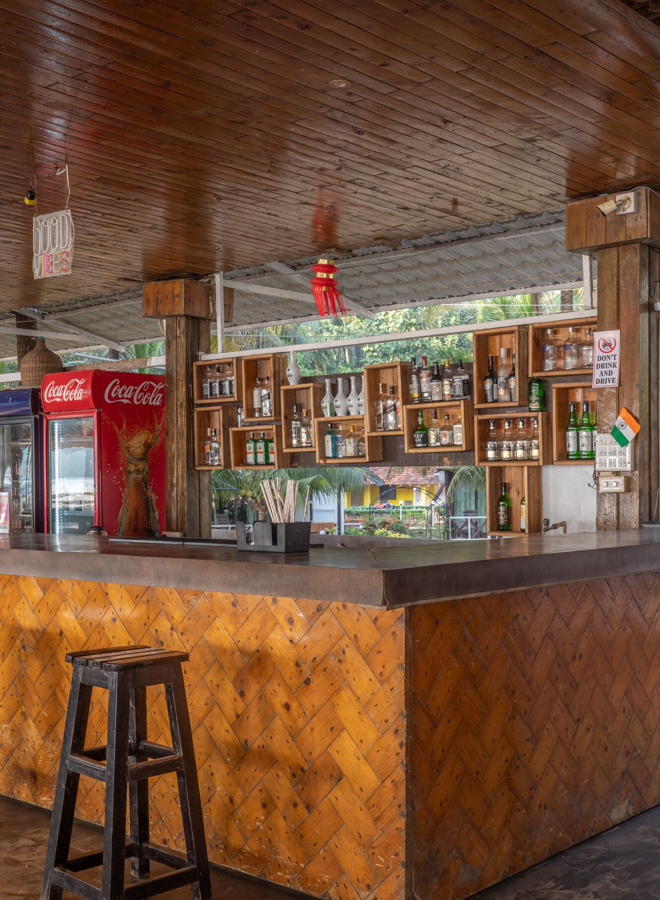 A bar area with wooden shelves displaying bottles and a Coca-Cola refrigerator.