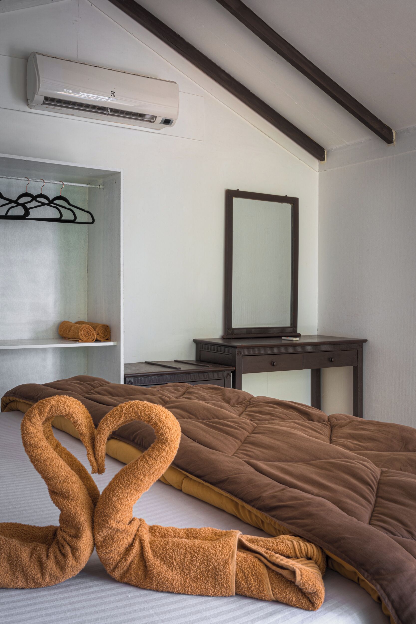 A hotel room with a bed, a mirror, a dresser, and an air conditioning unit.