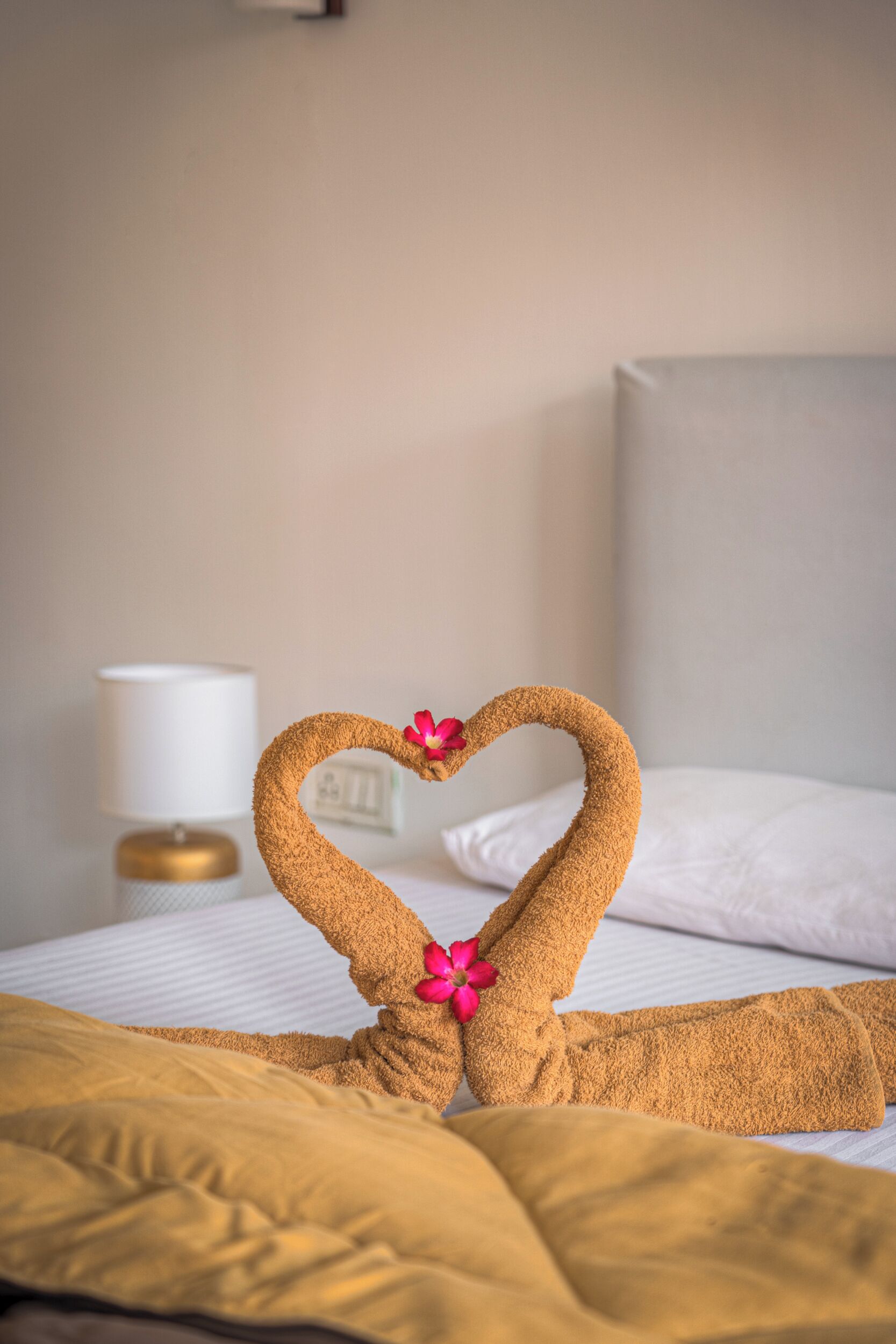 A bed with a towel arranged in a heart shape, a lamp, and a pillow.