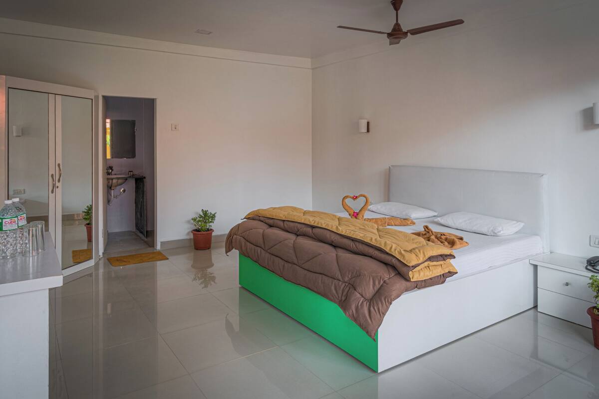 Un dormitorio moderno con una cama, una mesita de noche, un ventilador de techo y un baño visible a través de una puerta abierta.