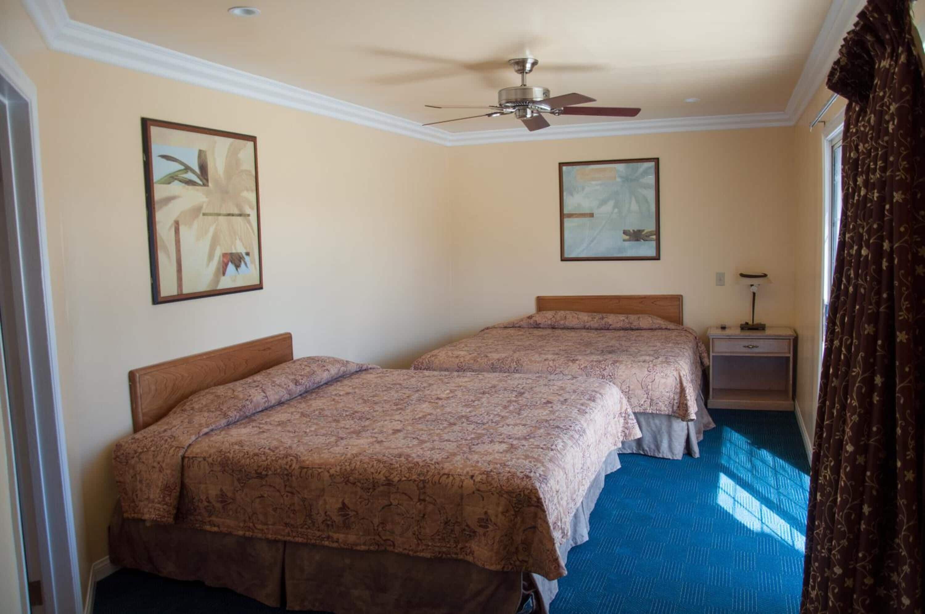 A hotel room with two beds, a ceiling fan, a nightstand, and a window with curtains.