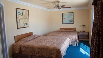 A hotel room with two beds, a ceiling fan, a nightstand, and a window with curtains.