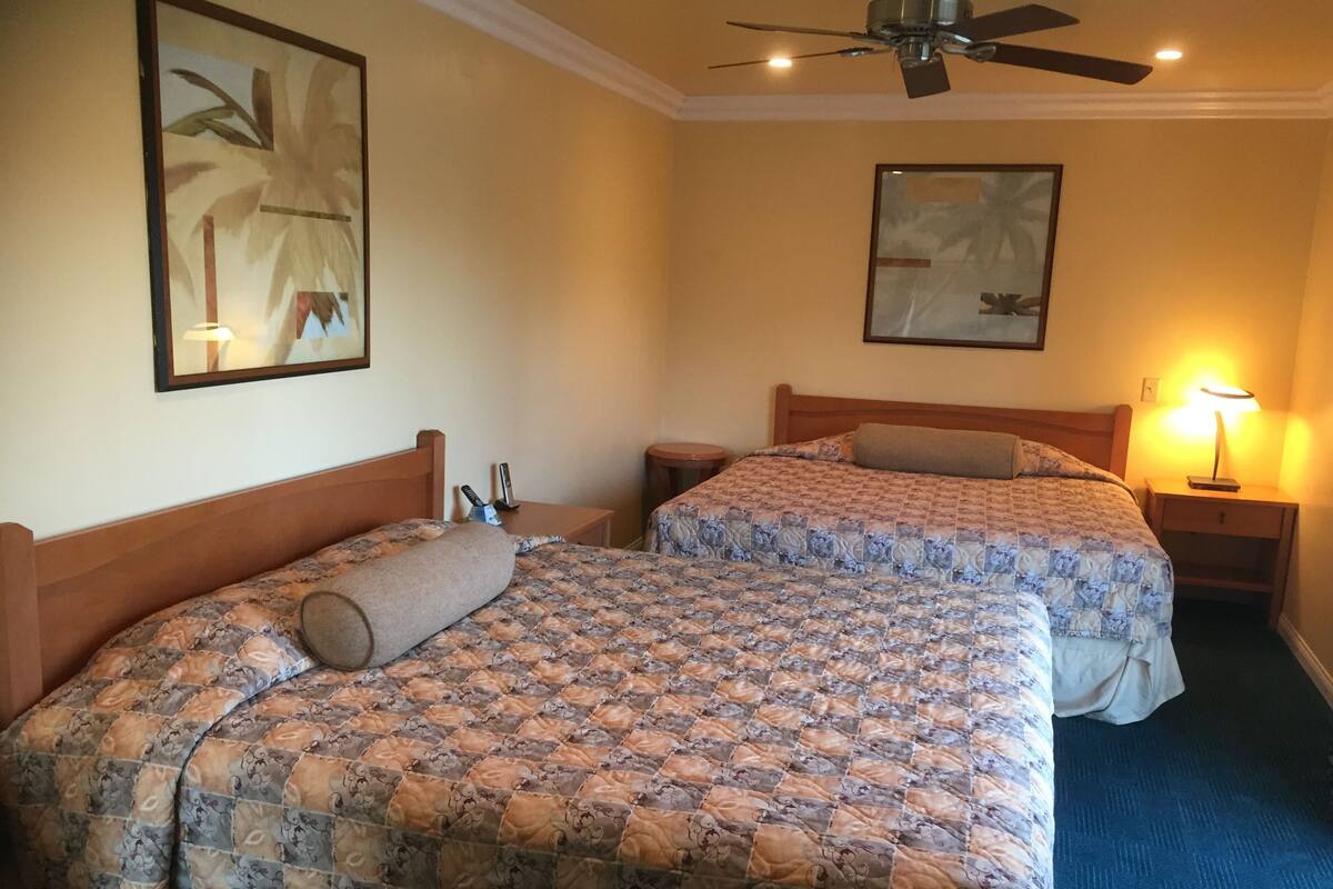A hotel room with two beds, a ceiling fan, and two bedside tables with lamps.